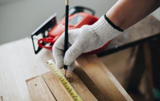 Main d'ouvrier avec un gant qui trace des mesures sur du bois
